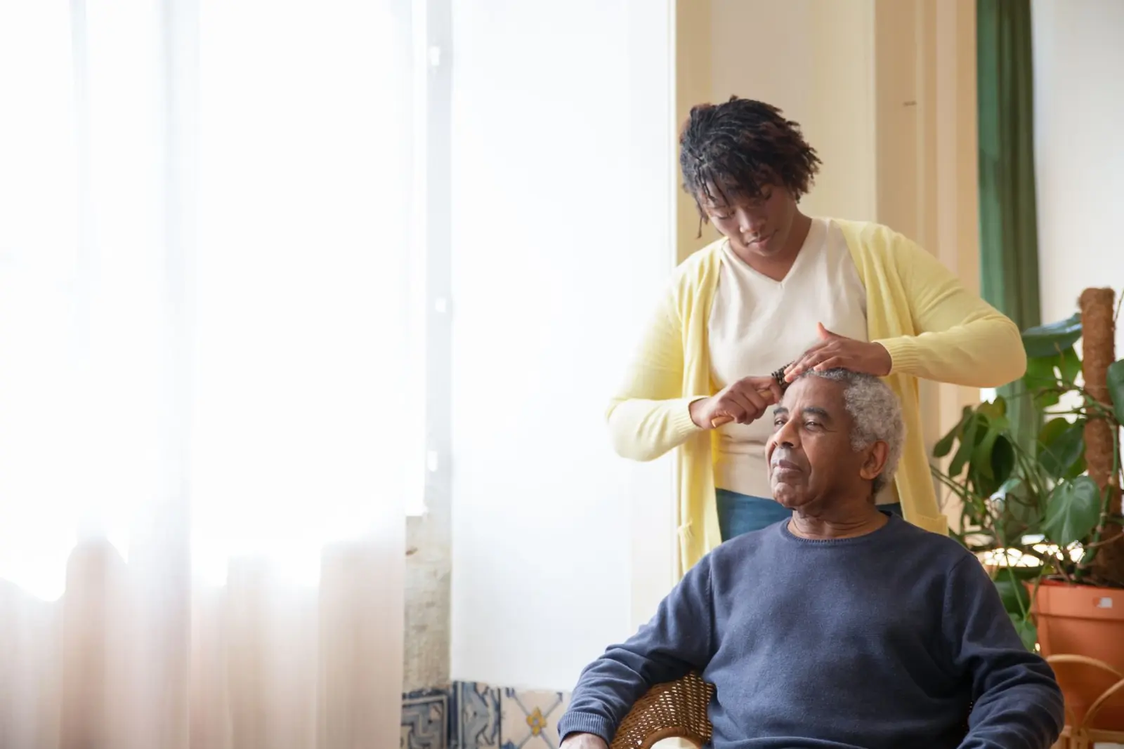 A caregiver gently styling an older man's hair in a sunlit room
